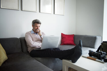 Seriöser Geschäftsmann, der einen Laptop benutzt, während er auf dem Sofa im Hotelzimmer sitzt - CAVF02999