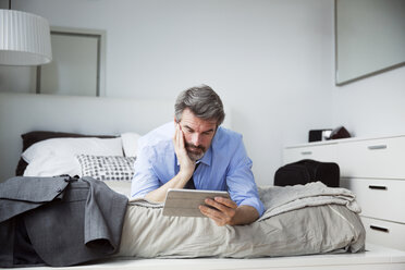 Geschäftsmann schaut auf Tablet-Computer, während er auf dem Bett im Hotelzimmer liegt - CAVF03009