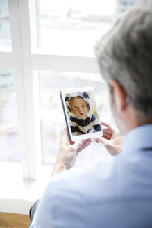 Rückansicht eines Mannes, der das Foto eines Babys auf seinem Smartphone betrachtet - CAVF03011