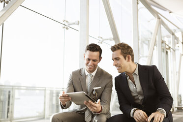 Happy businessmen using tablet computer while sitting on bench - CAVF03039