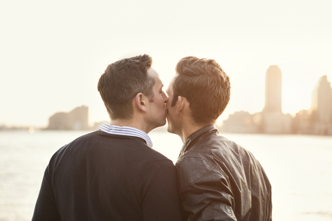 Mann küsst seinen Freund am Fluss gegen den klaren Himmel, lizenzfreies Stockfoto