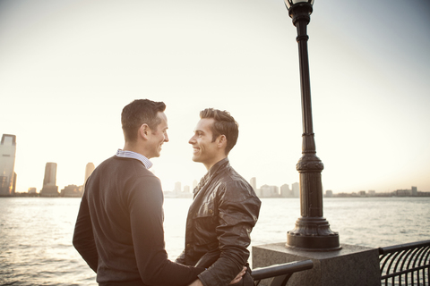 Glückliches homosexuelles Paar steht am Fluss gegen den Himmel, lizenzfreies Stockfoto