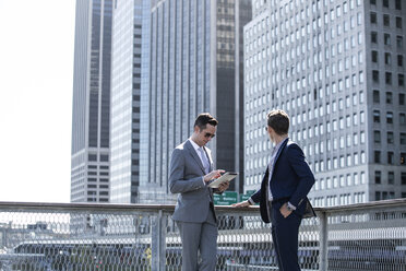 Businessman using tablet computer while standing friend against city buildings - CAVF03054