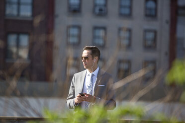 Young businessman listening to music while using phone in city - CAVF03057