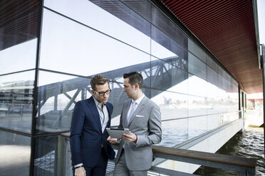 Geschäftsleute benutzen einen Tablet-Computer, während sie vor einem Gebäude stehen - CAVF03075