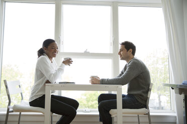 Male and female colleagues having coffee at table in office - CAVF03092