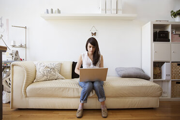 Woman using laptop while sitting on sofa at home - CAVF03114