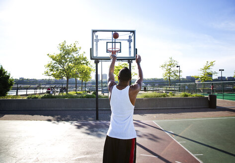 Rückansicht eines Sportlers, der an einem sonnigen Tag einen Basketball in einen Korb wirft - CAVF03126