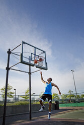 Man dunking ball in hoop at park against sky - CAVF03129