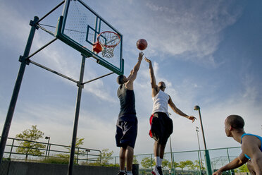 Low angle view of sportsmen playing basketball in court against sky - CAVF03138