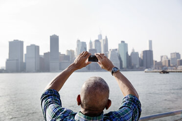 Rear view of senior man photographing city through smart phone by East River - CAVF03139