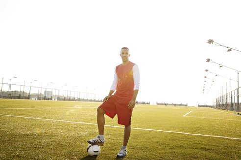 Porträt eines selbstbewussten Sportlers, der mit einem Ball auf einem Feld vor einem klaren Himmel steht - CAVF03143