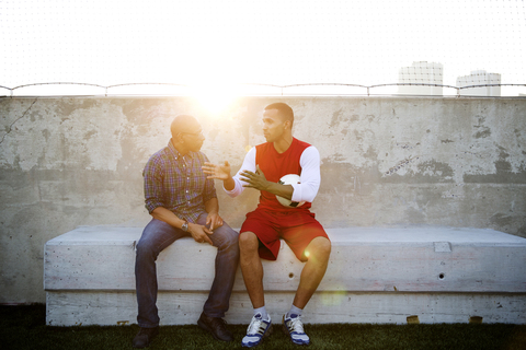 Fußballspieler im Gespräch mit seinem Vater, während er auf dem Platz sitzt, lizenzfreies Stockfoto