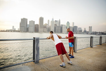 Vater im Gespräch mit einem Mann, der auf der Promenade am East River in der Stadt gegen den Himmel trainiert - CAVF03156