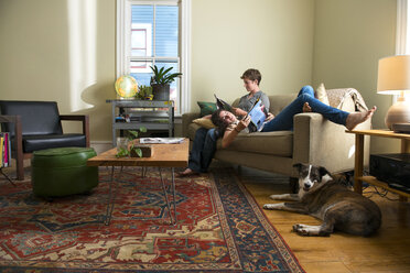 Lesbian couple reading magazine while relaxing on sofa at home - CAVF03181