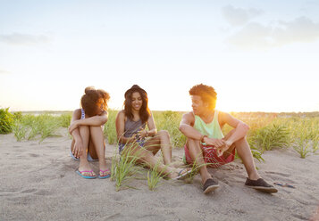 Glückliche Freunde, die am Strand sitzen und gegen den Himmel an einem sonnigen Tag kommunizieren - CAVF03198