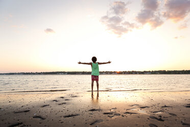 Rear view of man with arms outstretched standing at beach against sky at sunset - CAVF03200