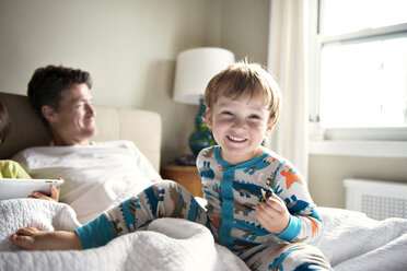 Happy boy enjoying with father while brother using tablet computer on bed at home - CAVF03227