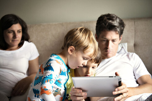 Woman looking at man using tablet computer with children on bed at home - CAVF03229