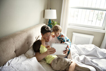 Father showing tablet computer to sons on bed at home - CAVF03230