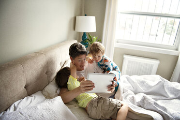 Vater zeigt Söhnen Tablet-Computer auf dem Bett zu Hause - CAVF03230