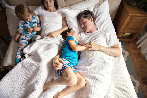 Draufsicht auf Eltern, die mit ihren Kindern zu Hause im Bett liegen, lizenzfreies Stockfoto