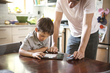 Father assisting son in using tablet computer at home - CAVF03235
