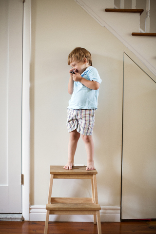 Glücklicher Junge auf einem Hocker stehend zu Hause, lizenzfreies Stockfoto