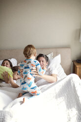 Glückliche Eltern spielen mit ihren Söhnen auf dem Bett liegend - CAVF03256