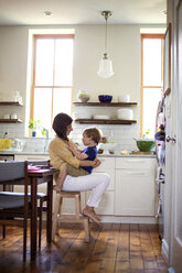 Son sitting on mother's lap in kitchen - CAVF03263