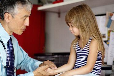 Doctor examining girl while holding her hand at home - CAVF03270