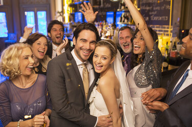 Freunde jubeln um das lächelnde Brautpaar bei der Hochzeitsfeier - CAIF08149