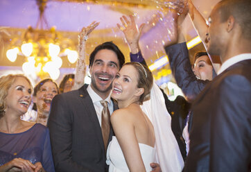 Freunde werfen Konfetti über Braut und Bräutigam beim Hochzeitsempfang - CAIF08153