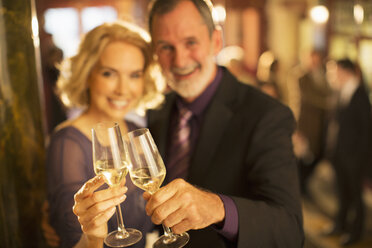 Portrait of well dressed couple toasting champagne glasses in theater lobby - CAIF08275