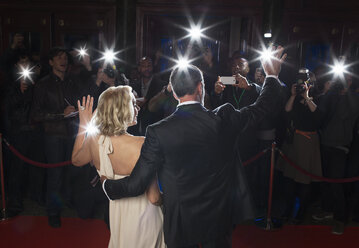 Rückansicht eines gut gekleideten Paares, das Paparazzi bei einer Veranstaltung auf dem roten Teppich zuwinkt - CAIF08318