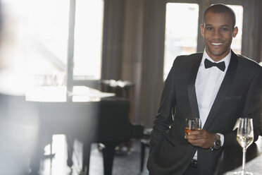 Porträt eines gut gekleideten Mannes, der in einer Lounge einen Cocktail trinkt - CAIF08393
