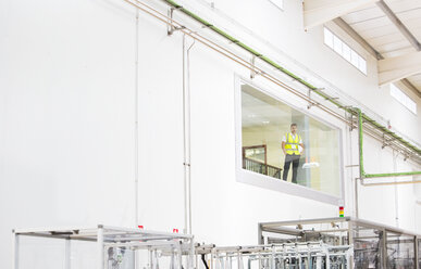 Worker looking out glass window in warehouse - CAIF08408