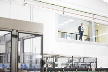 Geschäftsmann im Fenster mit Blick auf eine Fabrik - CAIF08420