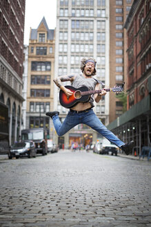 Mann springt beim Gitarrenspiel auf der Straße in der Stadt - CAVF03279