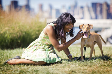 Frau spielt mit Hund, während sie auf einem Feld sitzt - CAVF03324
