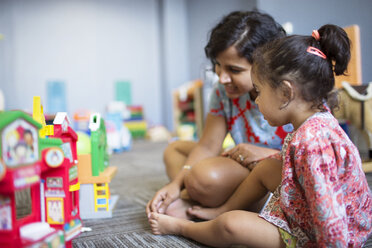 Mutter sitzt mit Mädchen beim Spielen mit Spielzeug zu Hause - CAVF03345
