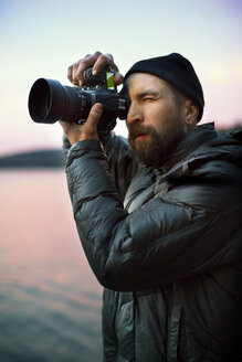 Man photographing while standing by lake during sunset - CAVF03402