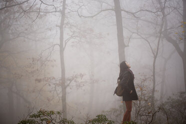 Side view of woman looking up while standing in forest - CAVF03456