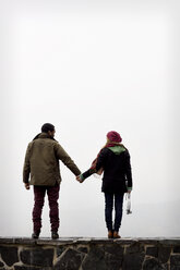 Rear view of couple standing on retaining wall against sky - CAVF03470