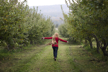 Rückansicht einer laufenden Frau im Obstgarten - CAVF03476