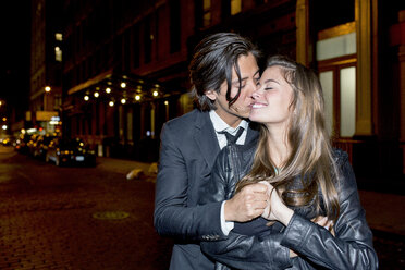 Romantic man kissing girlfriend while standing on city street at night - CAVF03480