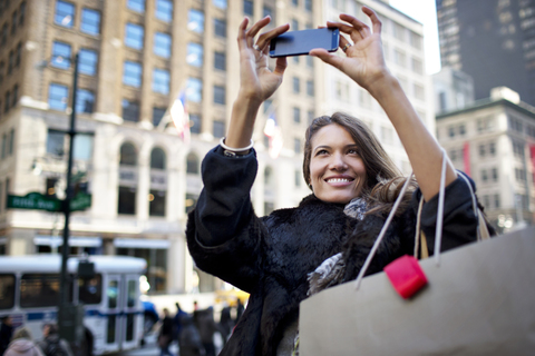 Frau nimmt Selfie, während gegen Gebäude in der Stadt stehen, lizenzfreies Stockfoto