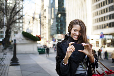 Woman photographing while standing on footpath in city - CAVF03539