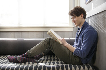 Seitenansicht eines lächelnden Mannes beim Lesen eines Buches zu Hause - CAVF03567