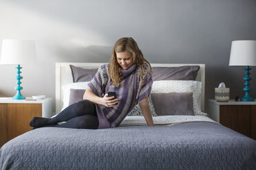 Woman using smart phone while sitting on bed at home - CAVF03569